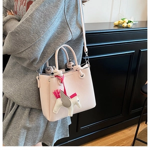 Lifestyle view of a pale pink textured leather tote bag with a decorative horse charm