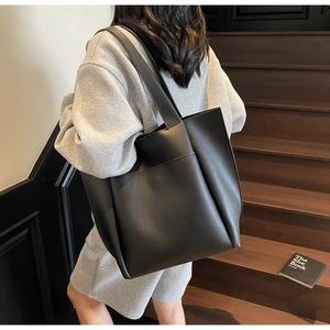 Detail of a large black leather tote bag with a front pocket on a casual model