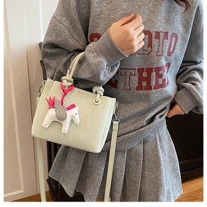 Detail of mint green bucket bag with Pegasus charm and pink tassel on crossbody strap