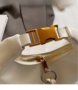 Close-up of golden metal buckle and zipper detail on white textured leather bag