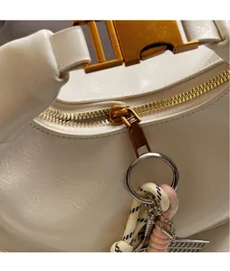 Close-up of polished gold zipper and woven charm on a white textured leather bag
