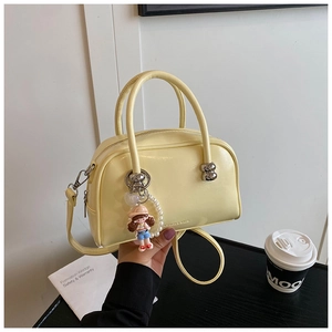 Detail of a creamy yellow pillow bag featuring golden ball hardware and doll charm