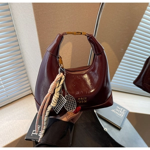 Macro shot of dark burgundy patent leather bag with gold buckle and tennis racket charm