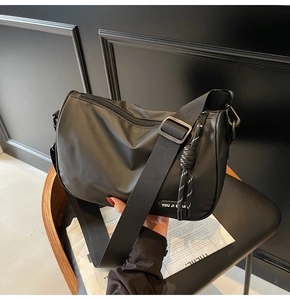 Detail of black crossbody bag showing rubber logo patch and smooth nylon texture