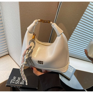 Detail of white patent leather crescent bag with golden buckle and metallic brand tag