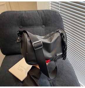 Detail view of a black nylon utility crossbody bag on a textured gray armchair