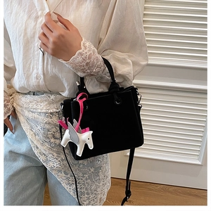 Detail of a black mini bucket bag featuring a white pegasus charm and adjustable strap