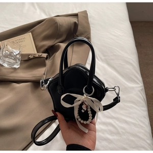 Detail of star-shaped black leather bag with white ribbon and pearl bear charm