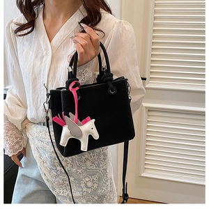 Close-up of black suede bucket bag featuring a pink pegasus charm and metal hardware