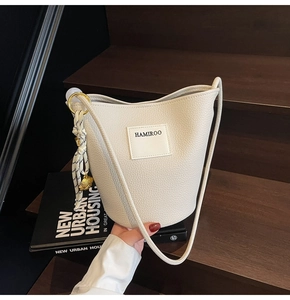 Détail d'un sac seau beige à texture de litchi posé sur un escalier en bois élégant