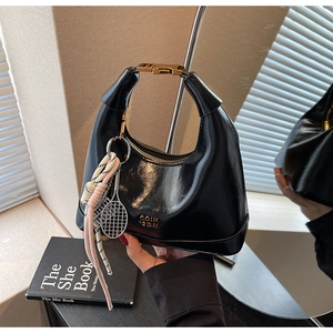 Detail of black glossy crescent bag with gold hardware and tennis racket charm pendant