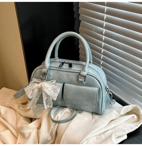 Detail of light blue crossbody bag with lace bow and pearl pendant on soft white fabric