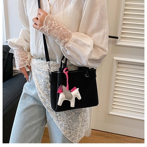 Detail of a black leather bucket bag featuring a white pegasus charm and crossbody strap