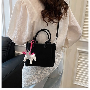 Detail of black crossbody bucket bag with white horse charm and adjustable strap