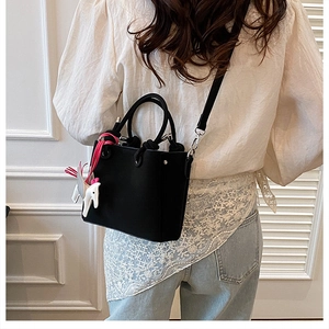 Detail of black leather bucket bag with creative white horse charm and crossbody strap