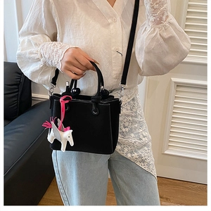 Detail of a black leather bucket bag featuring a white Pegasus charm and pink tassels