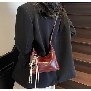 Detail view of burgundy half-moon handbag with gold logo and tennis racket charm