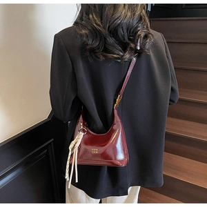 Detail of burgundy glossy leather dumpling bag featuring gold logo and rope charm
