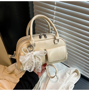 Detail of cream bowling bag featuring dual front pockets and a white lace bow charm