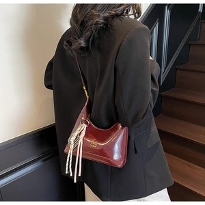 Close-up of retro burgundy hobo bag with glossy finish and tassel on wooden stairs