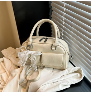 Detail of cream bowling bag with twin front pockets and delicate pearl lace bow charm