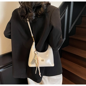 Detail view of cream dumpling shoulder bag with gold logo and decorative ribbon charm