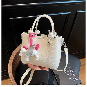 Detail of cream bucket bag with lychee leather texture and pink pony charm accessory