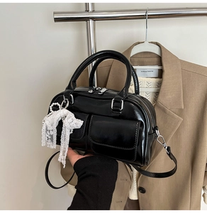 Detail of a black glossy bowling bag featuring lace bow, pearl charm, and double front pockets