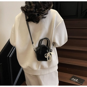 Detail of mini black leather star bag featuring a pearl chain and white bow pendant