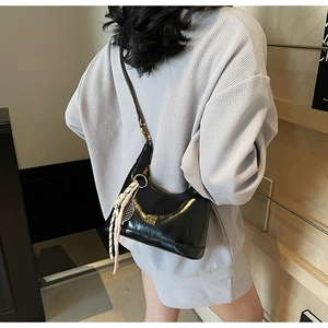 Detail of black glossy croissant bag with woven strap and gold logo worn as crossbody