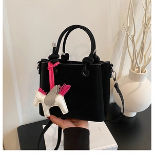 Close-up of black matte bucket bag with a decorative pegasus pendant and woven rope handle