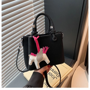 Detail of black matte leather tote bag featuring a white Pegasus charm and pink tassel