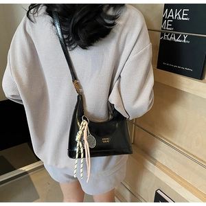 Close-up of black glossy patent leather shoulder bag with a unique sports-style charm