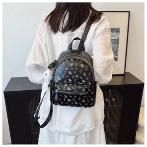 Détail d'un mini sac à dos noir avec imprimé floral violet et breloque boule en peluche