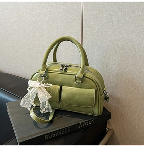 Close-up of sage green leather bowling bag with twin pockets and lace bow detail