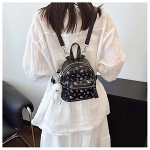 Détail d'un mini sac à dos noir à fleurs avec motifs roses et pendentif peluche