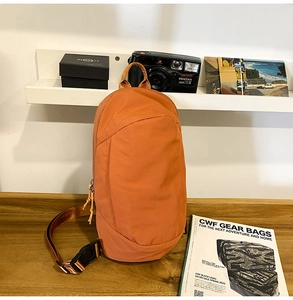Detail of orange water-resistant crossbody bag with adjustable strap on wooden table