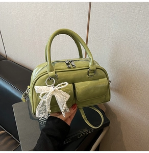 Close-up of grass green bowling bag with white lace bow and pearl pendant detail