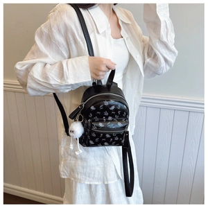 Détail d'un mini sac à dos noir fleuri avec nœuds et pendentif en peluche blanche