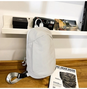 Close-up of lightweight light grey nylon crossbody bag on a wooden table with camera