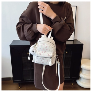 Détails d'un mini sac à dos blanc à motifs floraux avec pendentif en peluche et zip en métal