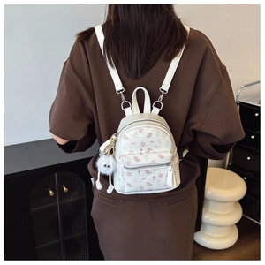 Gros plan d'un mini sac à dos blanc fleuri avec nœuds et pendentif en peluche sur le dos