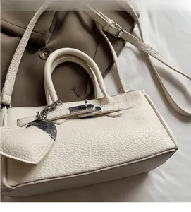 Detailed view of white lychee leather handbag featuring classic metal lock and heart charm