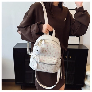Détail d'un sac à dos à fleurs avec zips argentés et breloque blanche sur sweat marron