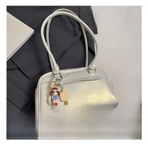 Detailansicht der perlweißen Achseltasche mit niedlichen Anhängern auf einem grauen Sakko