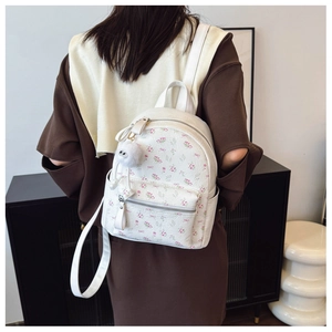 Vue détaillée du sac à dos fleuri avec motifs en relief et pendentif boule en peluche