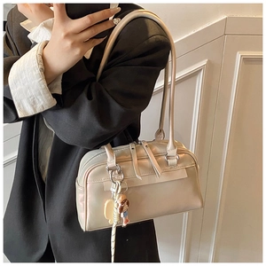 Detail einer perlmuttfarbenen beigen Schultertasche mit Reißverschluss und Anhänger