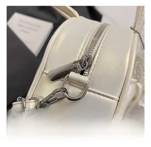 Detailed close-up of silver metal zipper and spring hook on the cream pleated bag
