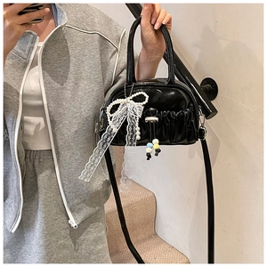 Detail of black patent leather Boston bag with pleated design and pearl lace bow