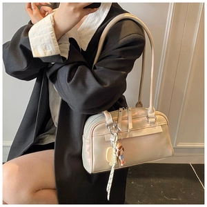 Elegante cremeweiße Boston Tasche mit Schultergurt und Plüsch-Anhänger am Modell
